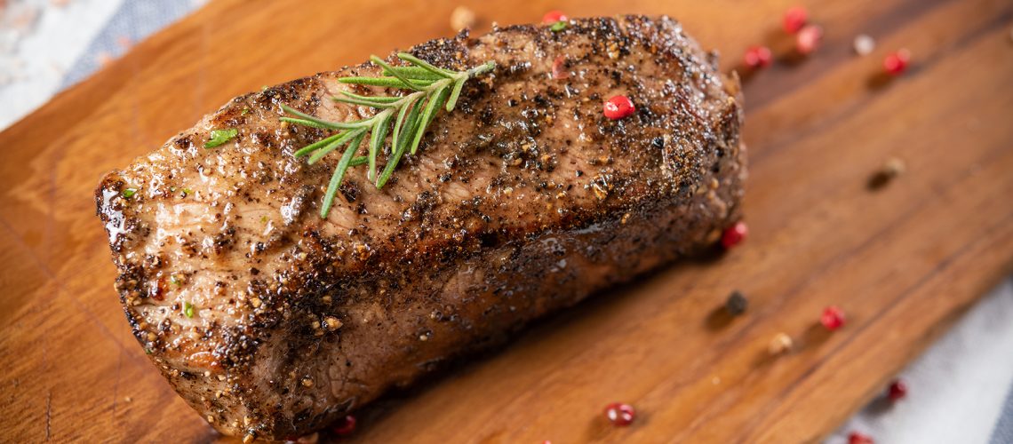 Full piece of beef steak with black pepper, not yet cut on a wooden chopping board with rosemary leaves and many spices, beautiful decorated, gray-white napkin background. Good food for good health